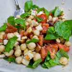alt="a salad featuring cooked chickpeas, tomatoes, roasted almonds, preserved tofu, and lots of fresh Italian basil."