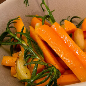 alt="orange carrots, green rosemary, and roasted garlic beautifully presented in an oval bowl."