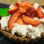 alt="a beautifully presented dessert of vanilla ice cream, fresh strawberries and mint served on top of a large almond oatmeal cookie."