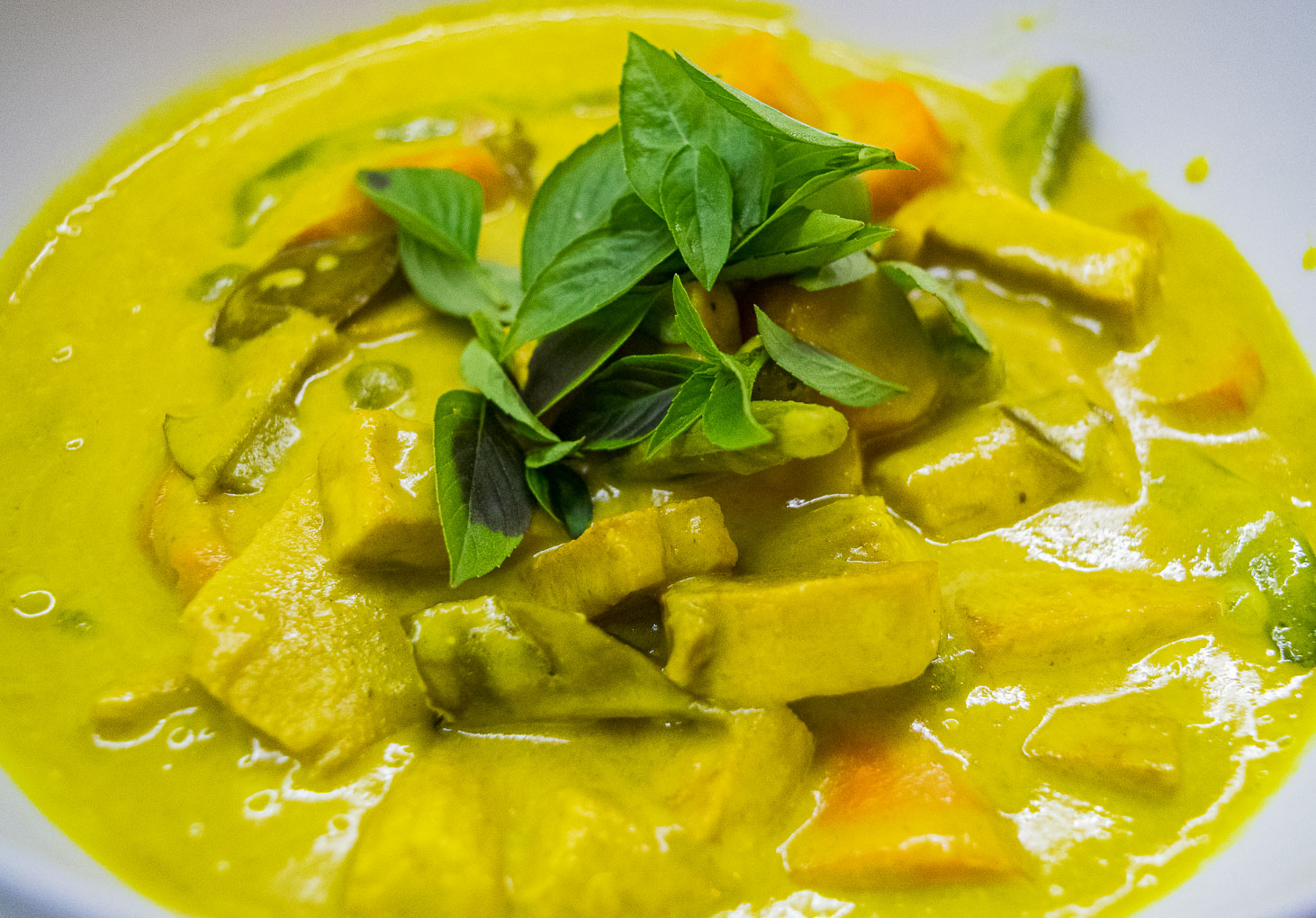 alt="brightly colored yellow curry decorated with green Thai basil."