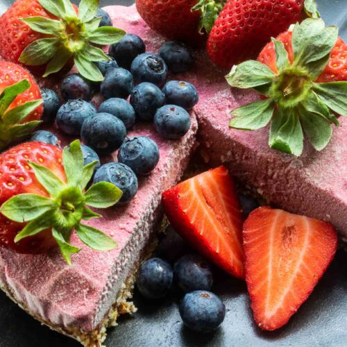 alt="a frosty looking strawberry ice cream cake topped with fresh blueberries and strawberries."