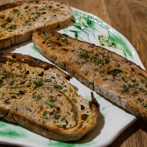 alt="slices of sourdough bread sprinkled with rosemary and drizzled with olive oil."