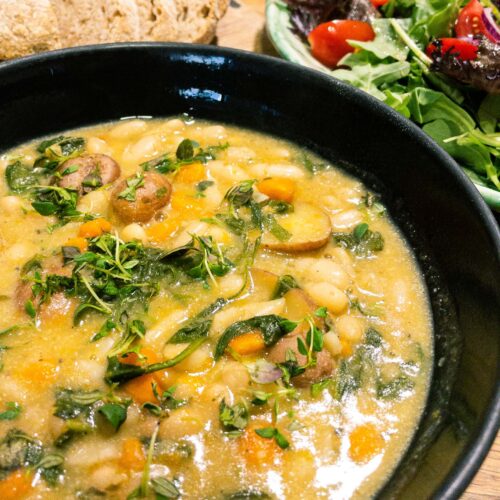 alt="a bowl of white beans and potato soup served with a mixed salad and sourdough bread."