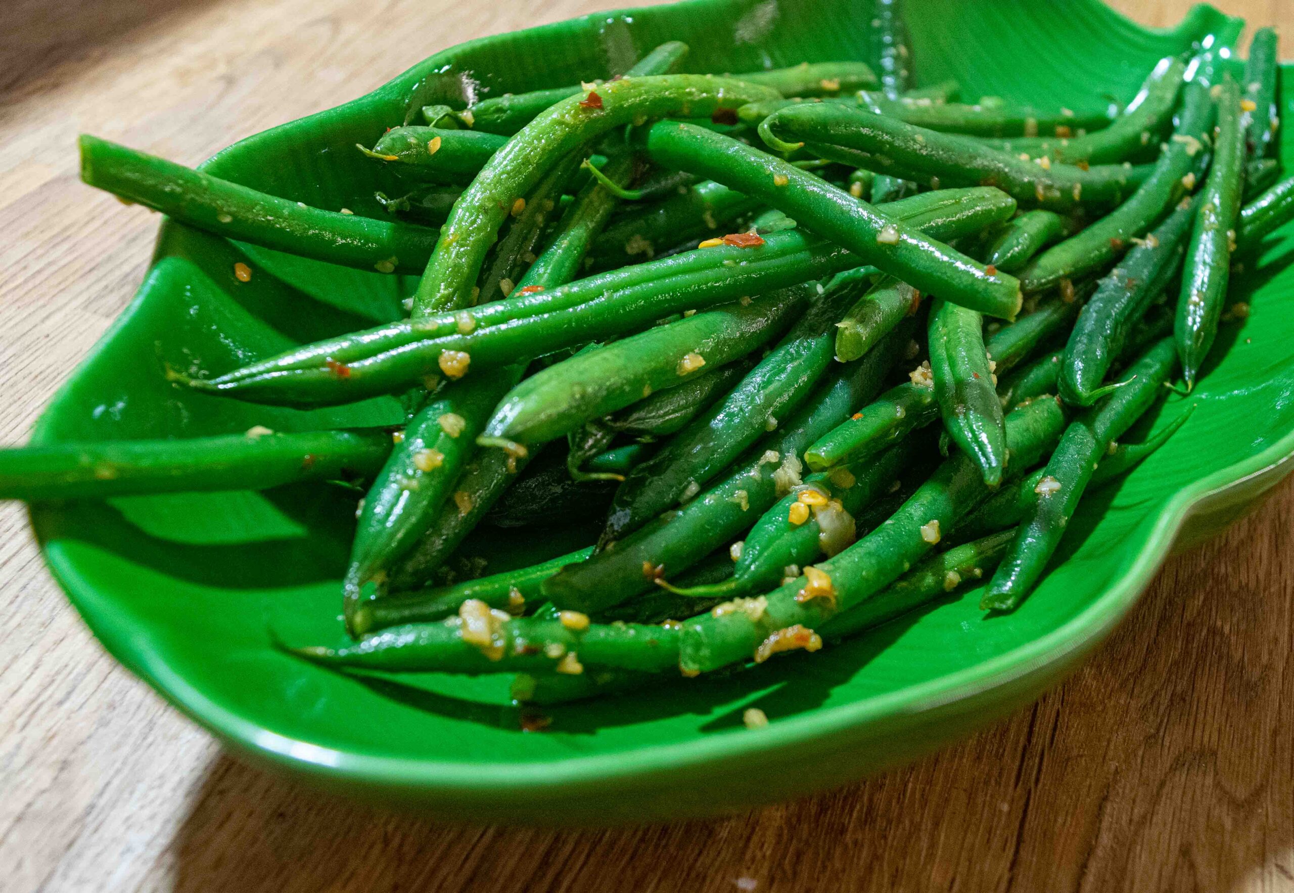 alt="stir-fried green beans with garlic and chili served on a ceramic palm leaf plate."