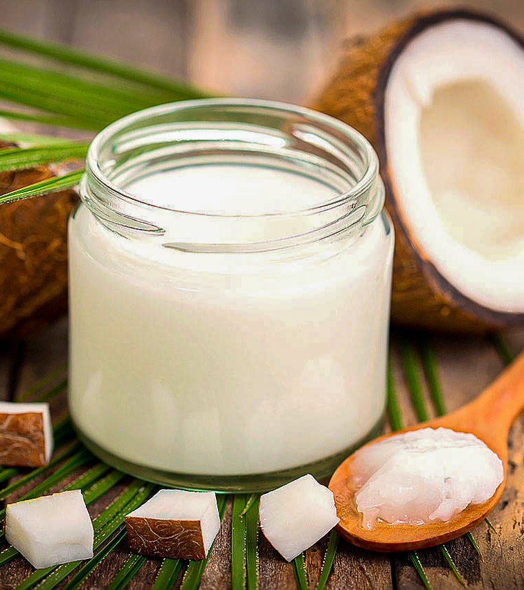 A jar of coconut oil on a palm leaf with a halved coconut in the background. 