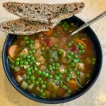 alt="chunky vegetable soup served with two slices of sourdough bread."