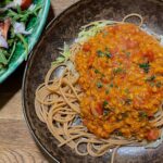 alt="red lentil Bolognese sauce over whole wheat spaghetti. A mixed salad is served on the side."
