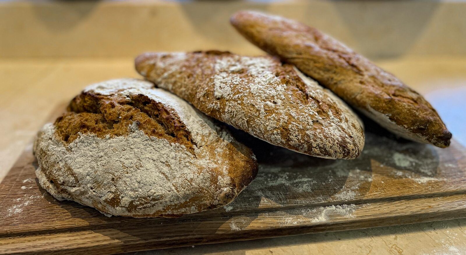 Three crusty sourdough breads on a chopping board.