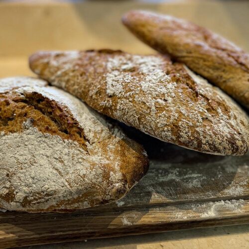 alt="three crusty sourdough breads on a chopping board."