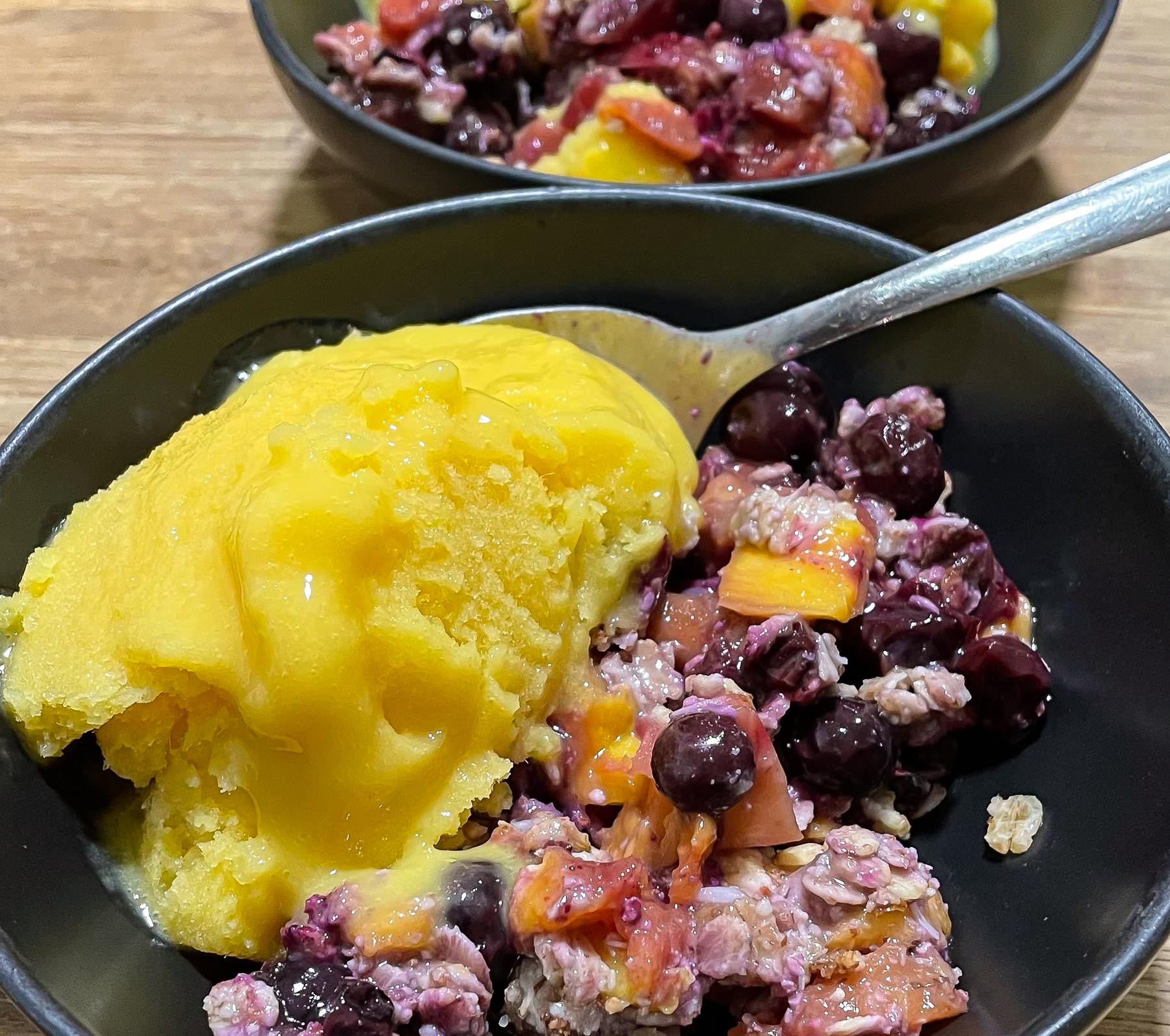 alt="a bowl with mango and blueberry cobbler topped with mango ice cream."