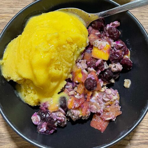alt="a bowl with mango and blueberry cobbler and topped with mango ice cream."