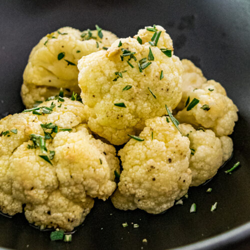 alt="roasted cauliflower sprinkled with fresh rosemary." Served in a black bowl.