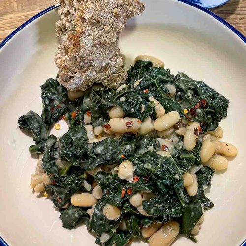 alt="white beans and kale served with sourdough and extra chili flakes on the side."