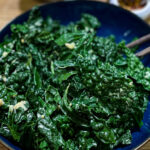 alt="deeply green Tuscan kale drizzled with zesty dressing and served in a dark blue bowl."