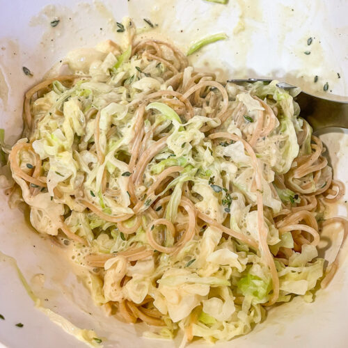 alt="a close up of a bowl of spaghetti alfredo with thinly sliced cabbage and fresh thyme."