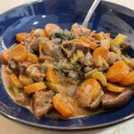 alt="a dark blue bowl with mushroom Bourguignon in orange, green, brown, and yellow colors."