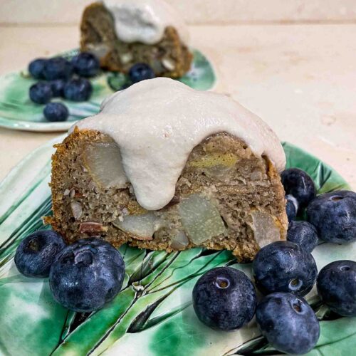 alt="a slice of pear cake topped with pear cream, served with blueberries."