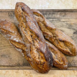 alt="four perfect looking whole spelt sourdough baguettes on a chopping board."