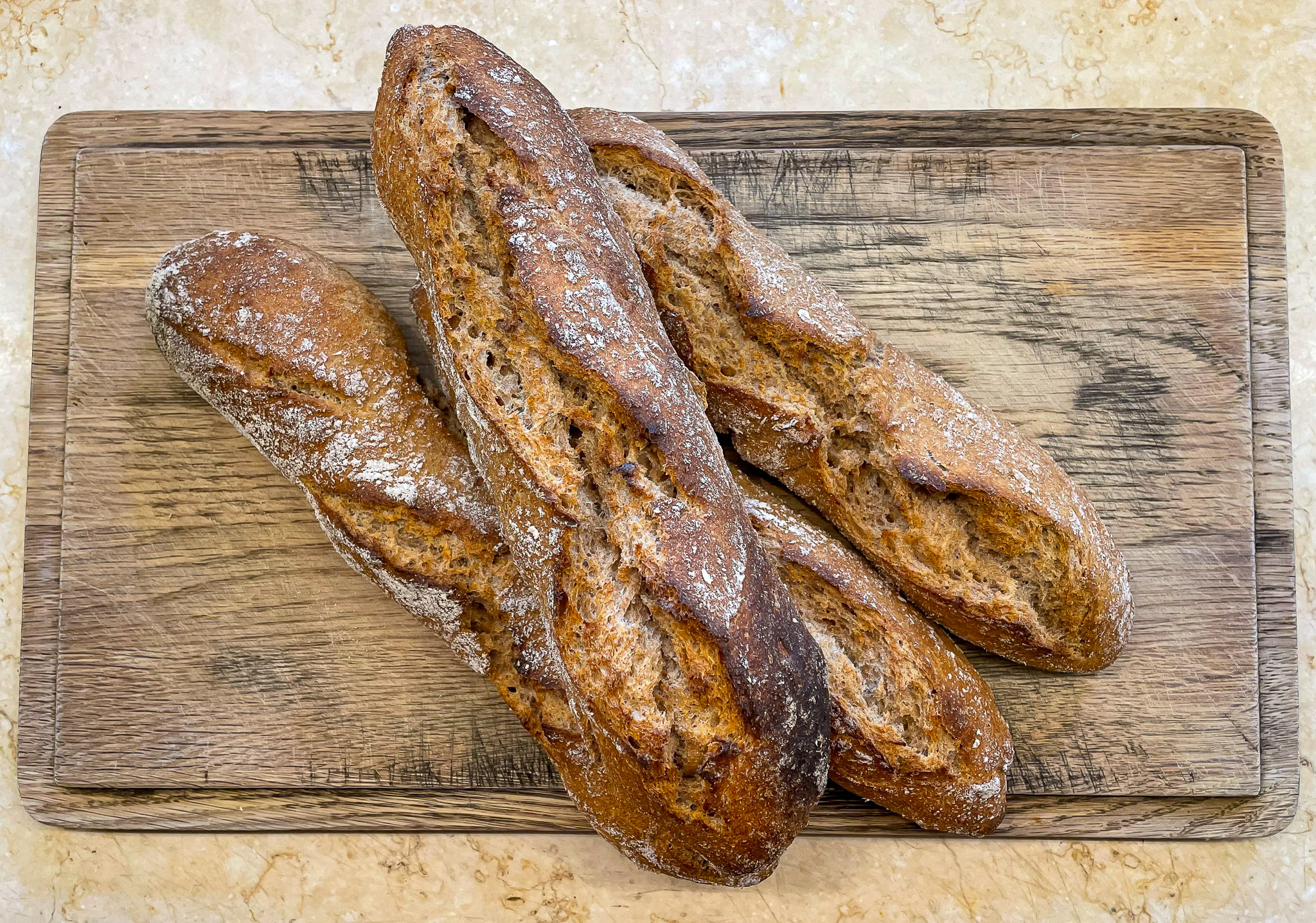 alt="four perfect looking whole spelt sourdough baguettes on a chopping board."