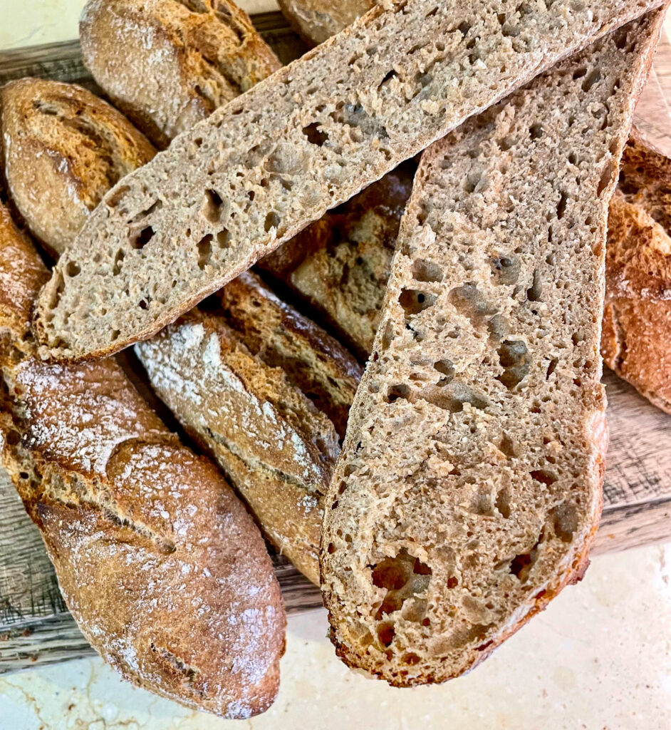 A whole grain spelt sourdough baguette that has been sliced in half lengthwise to show the classic voids characteristic of traditional sourdough breads.