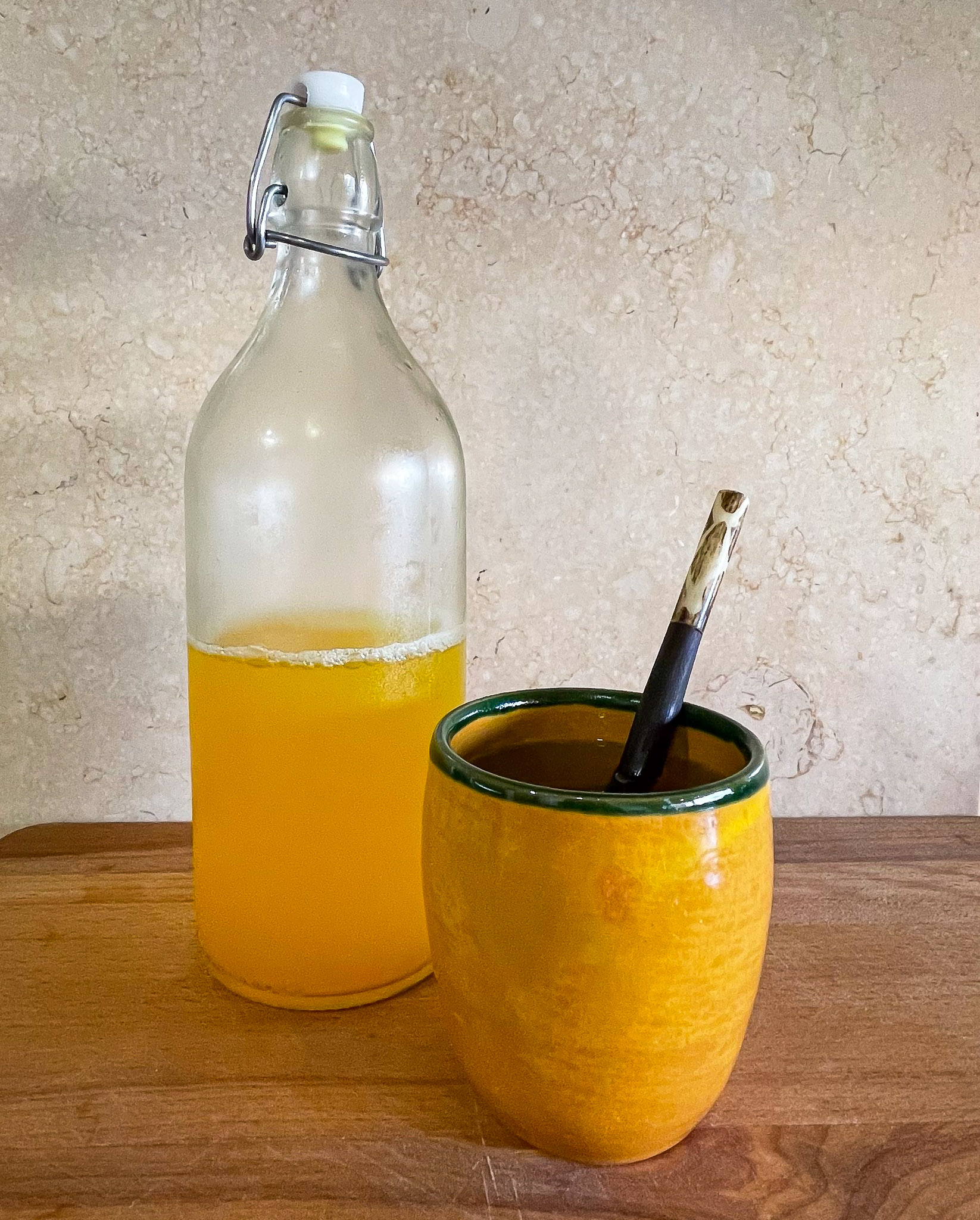 alt="a yellow ceramic mug containing a liquid set in front of a glass bottle containing the yellow winter tonic."