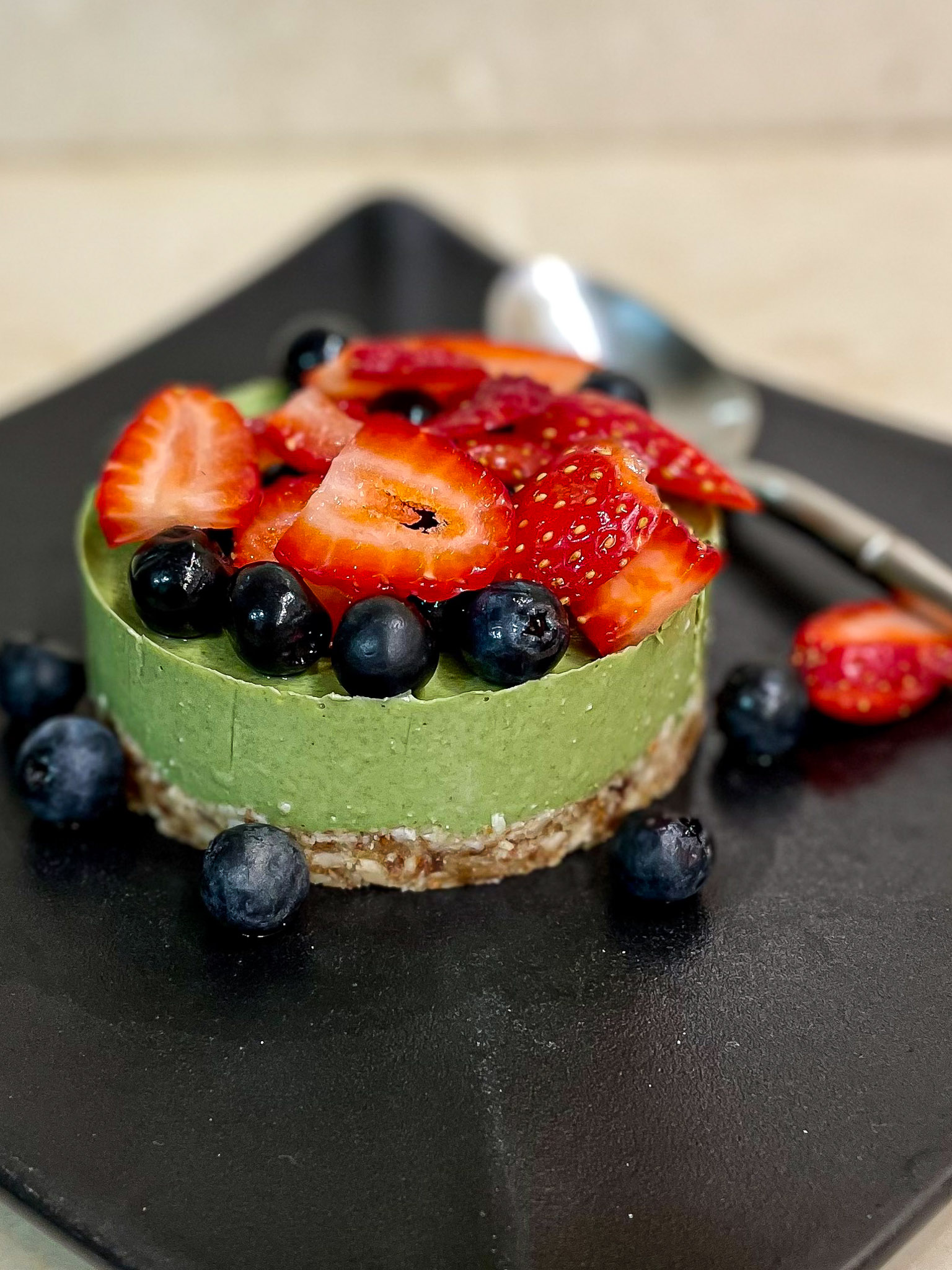 alt="a very green matcha mousse cake topped with fresh strawberries and blueberries."