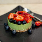 alt="a very green matcha mousse cake topped with fresh strawberries and blueberries."