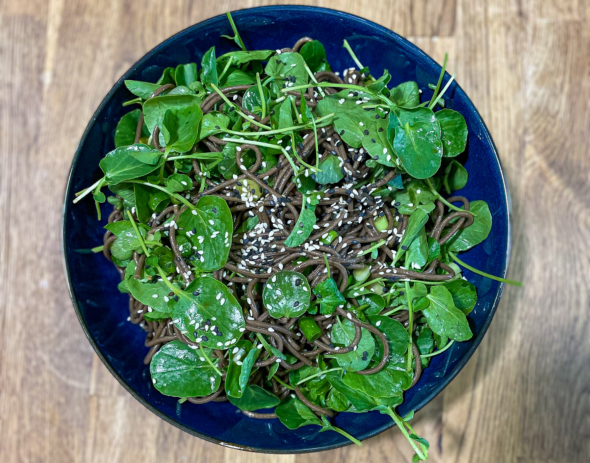 alt="a blue bowl full of soba noodle salad with lots of fresh green watercress."