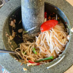 alt="green papaya salad in the process of being made using a mortar and pestle."