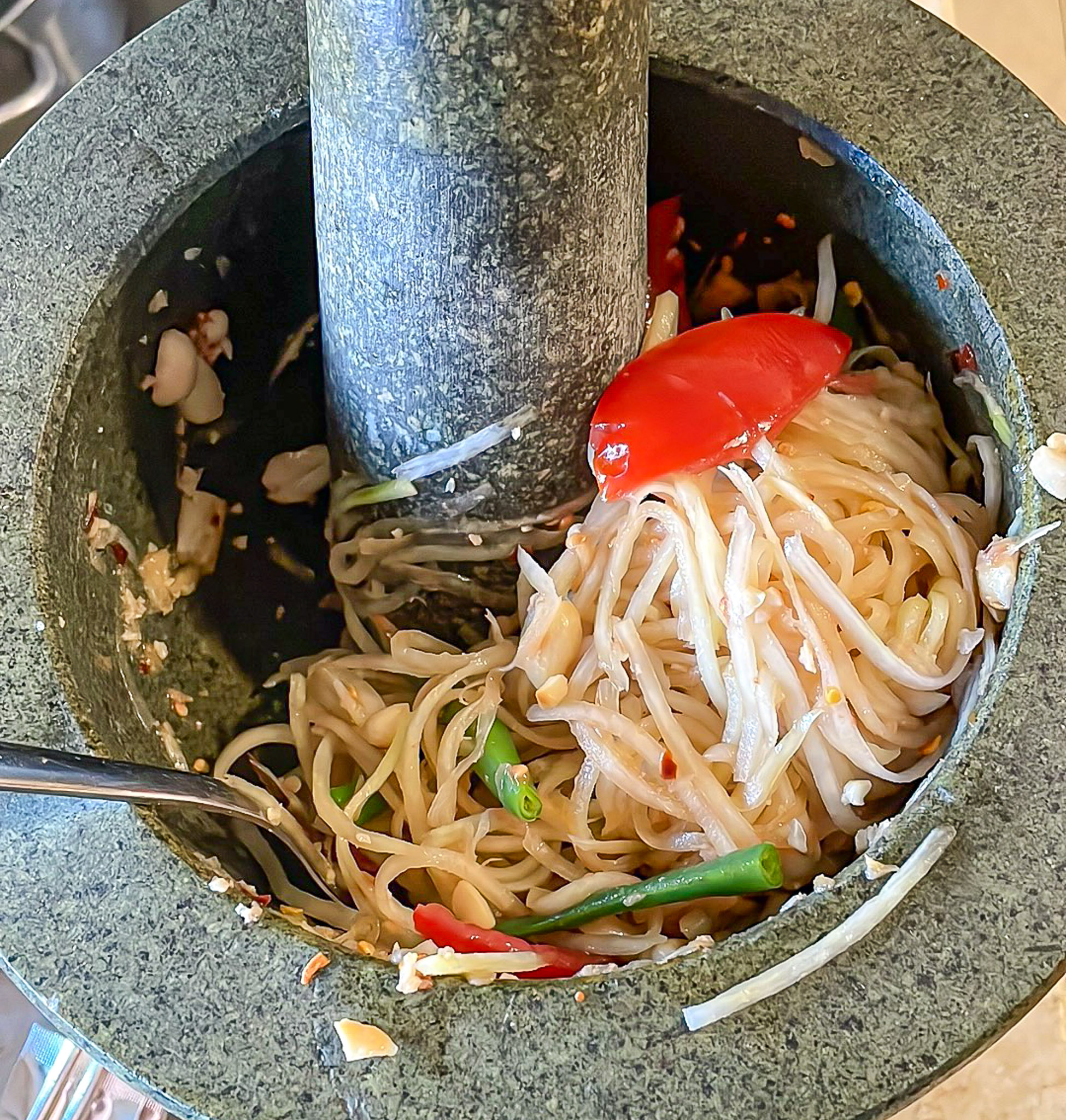 alt="green papaya salad in the process of being made using a mortar and pestle."