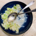 alt="a half eaten bowl of white cabbage in bechamel sauce served in a blue bowl."