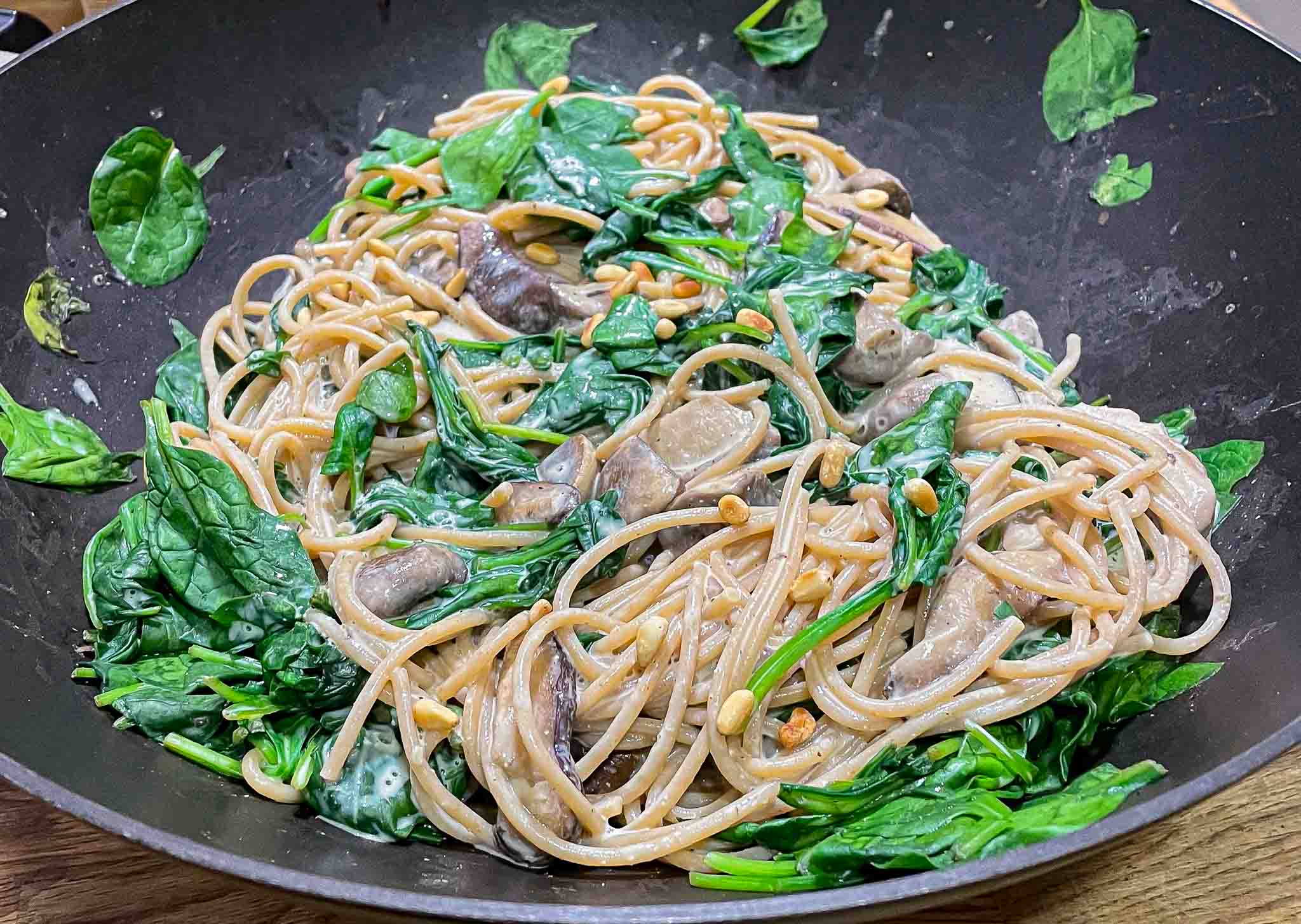 alt=a bowl with spaghetti with in light cream sauce with mushrooms, spinach, and roasted pine nuts."
