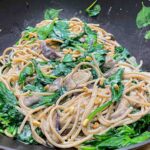 alt=a bowl with spaghetti with in light cream sauce with mushrooms, spinach, and roasted pine nuts."