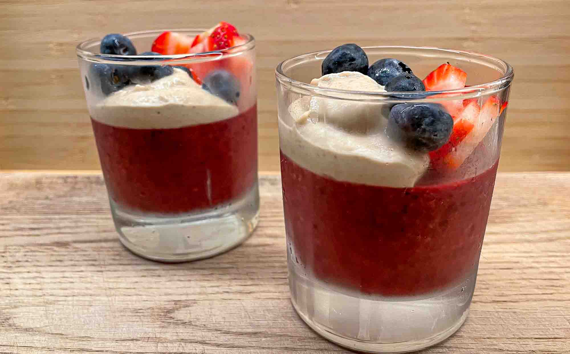 alt="an individual portion of berry pudding with some strawberry slices, blueberries, and a dollop of rich cashew cream on top."