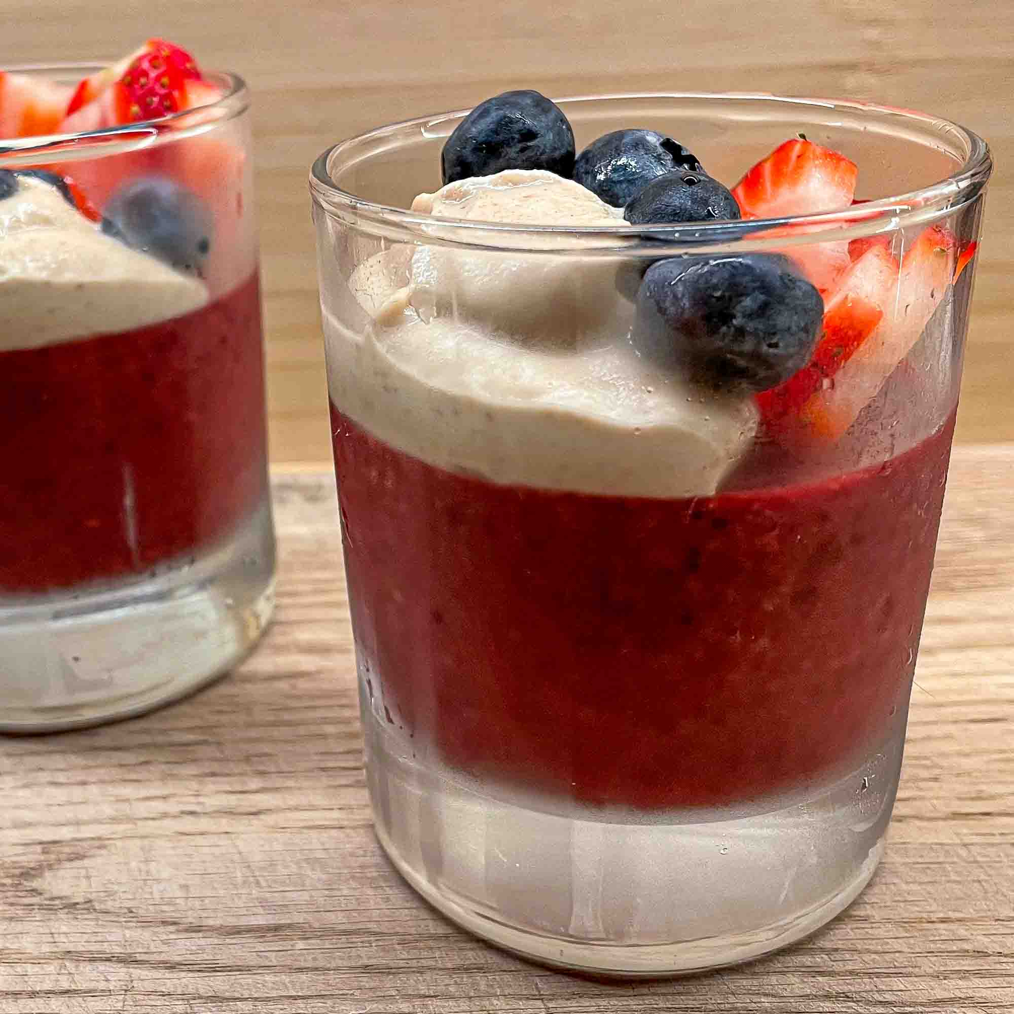 alt="an individual portion of berry pudding with some strawberry slices, blueberries, and a dollop of rich cashew cream on top."